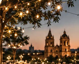 Cena al aire libre con luces colgantes y una catedral al fondo